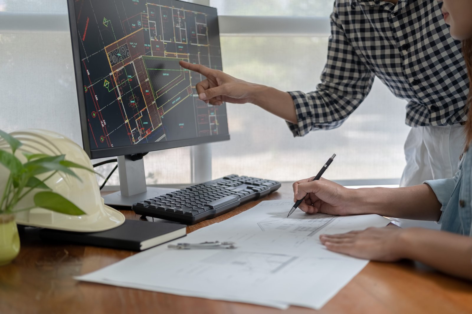 Engineers discuss a blueprint while checking information on a tablet computer in a office.